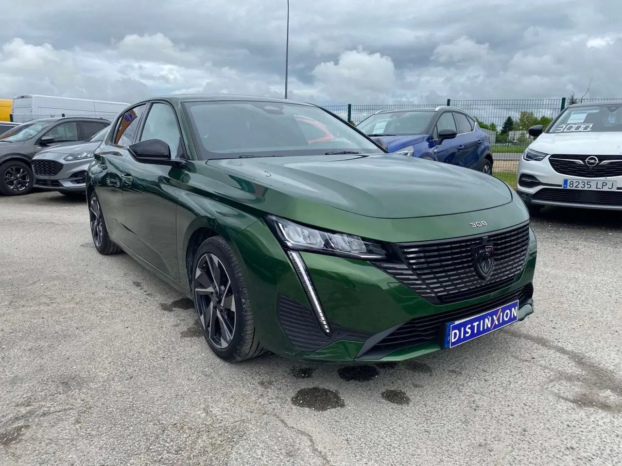 Peugeot 308 Vert Olivine vue 3/4 avant avec calandre noire et feux LED verticaux distinctifs.