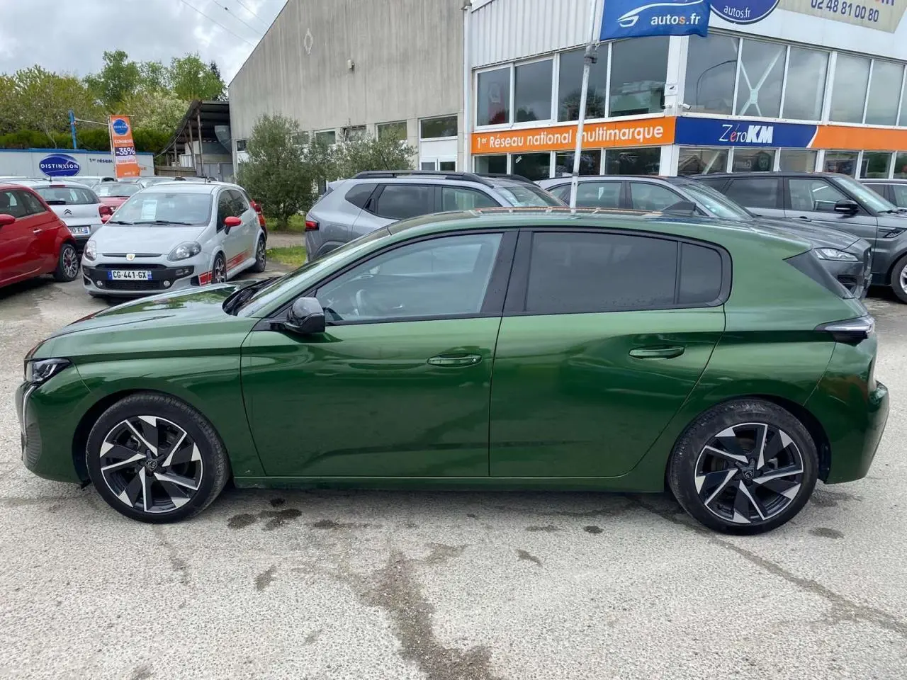 Profil latéral droit d'une Peugeot 308 2023 vert olivine avec jantes alliage 17 pouces et vitres surteintées.