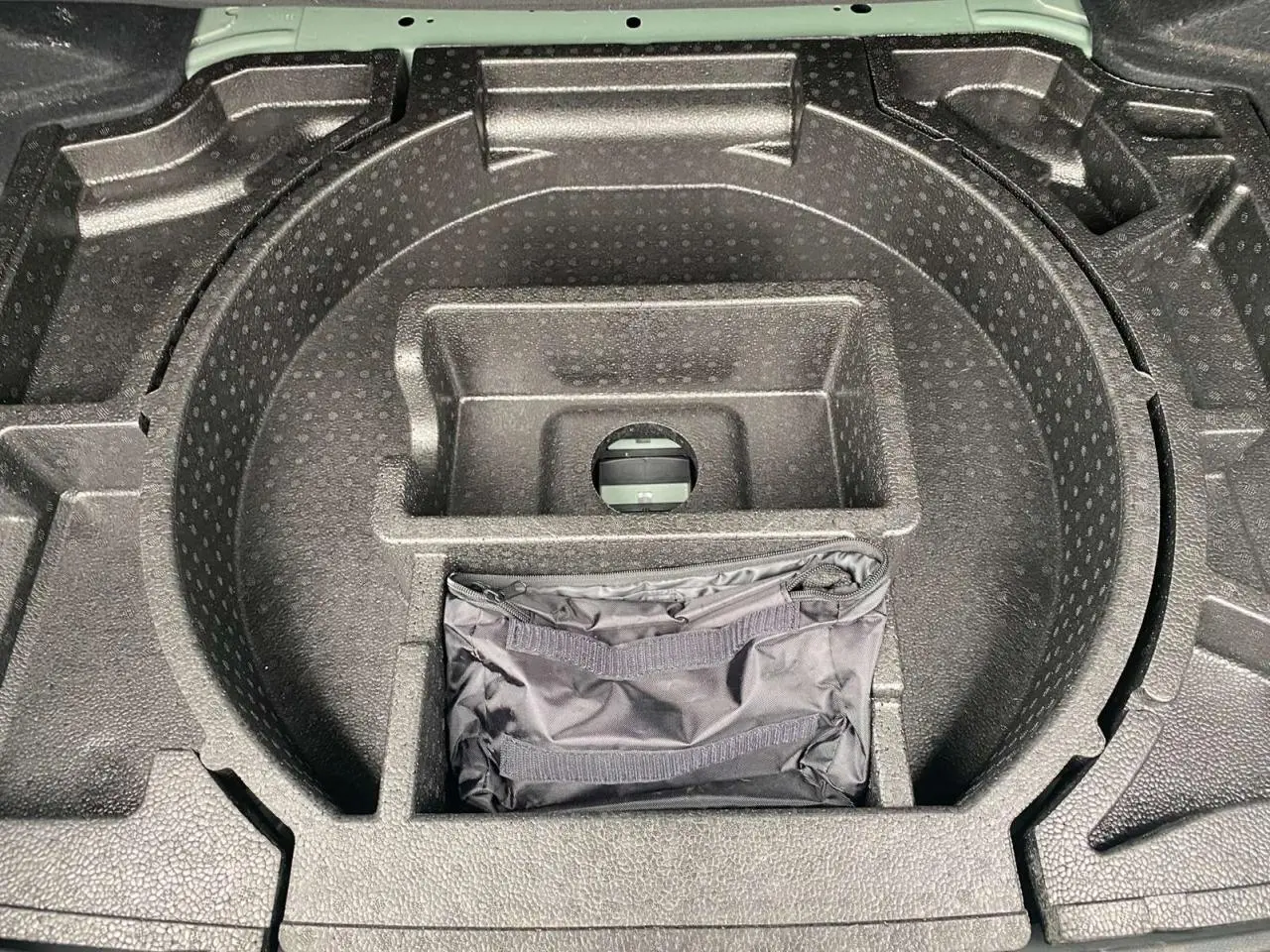 Rangement de coffre en mousse noire avec sacoche, partie arrière d'une Peugeot 308 Vert Olivine 2023 visible au fond.