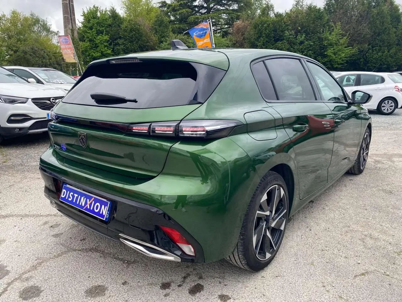 Vue 3/4 arrière droite d'une Peugeot 308 2023 vert olivine avec jantes alliage et vitres surteintées.
