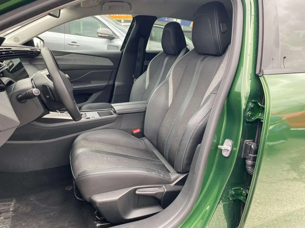Vue côté gauche intérieur de la Peugeot 308 2023 vert olivine, sièges avant en cuir et tissu gris avec console centrale.