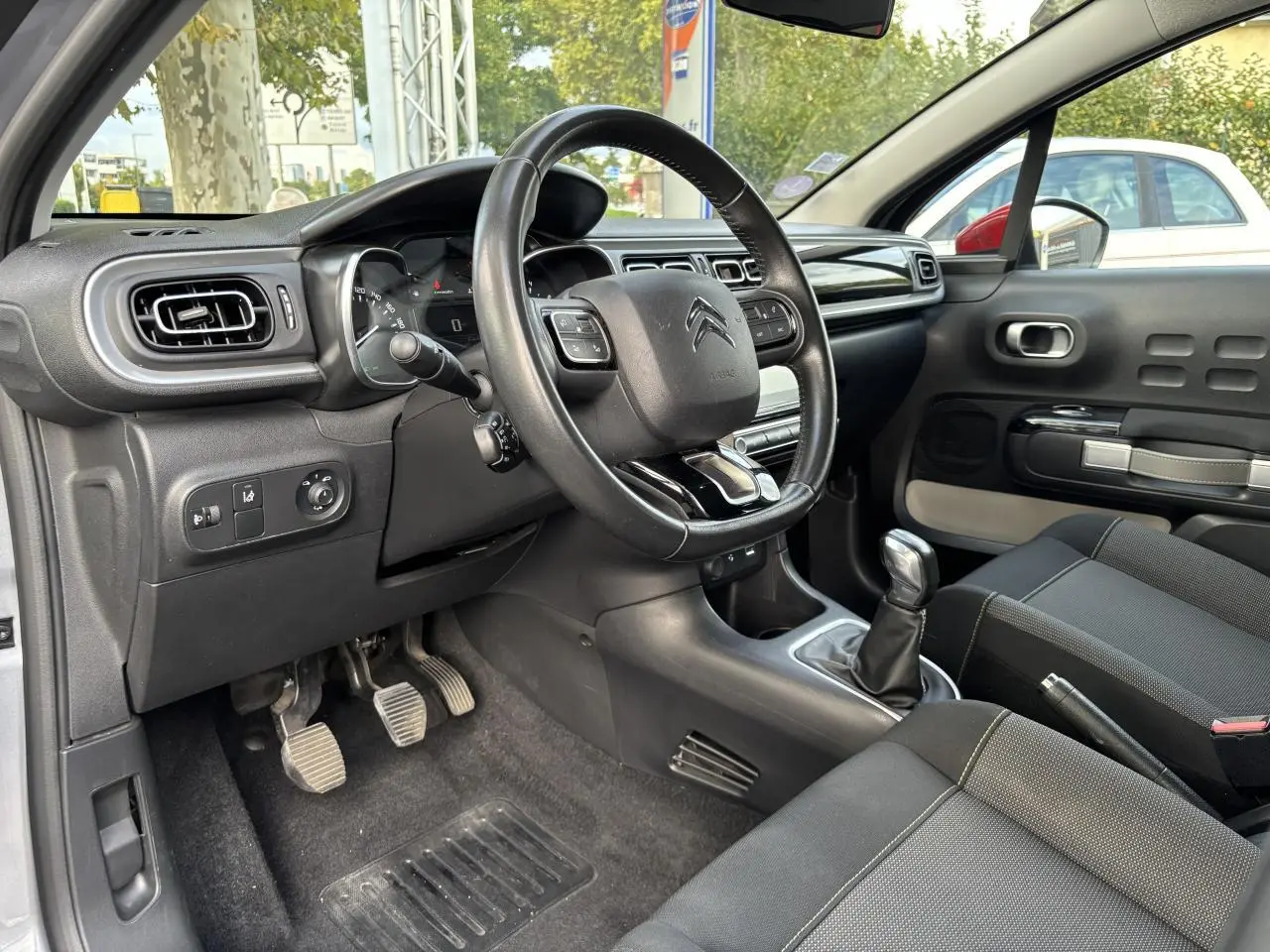 Intérieur de Citroën C3 2019 côté conducteur, volant multifonction, levier de vitesse manuel et sièges noirs.