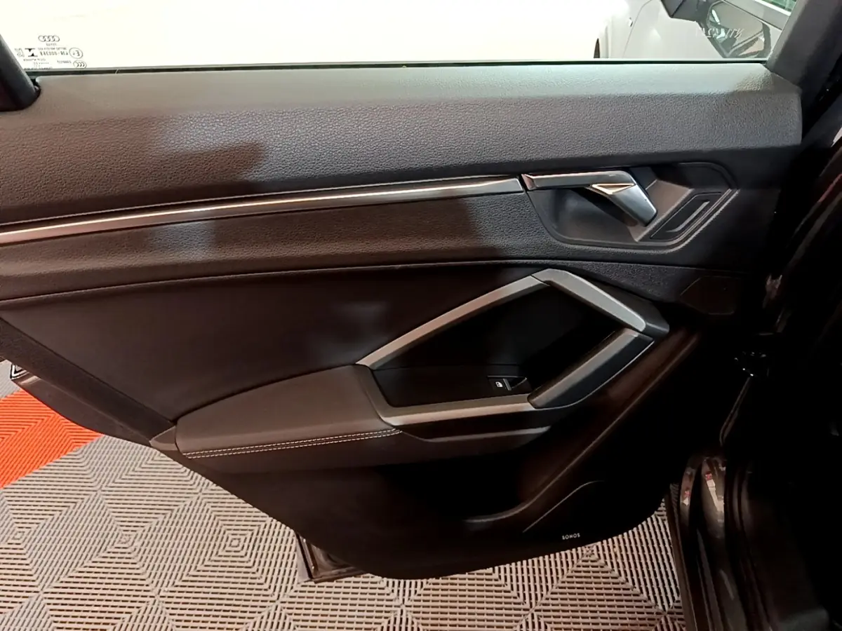 Vue intérieure côté gauche de la porte avant d'un Audi Q3 gris foncé avec garniture noire et insert argenté.