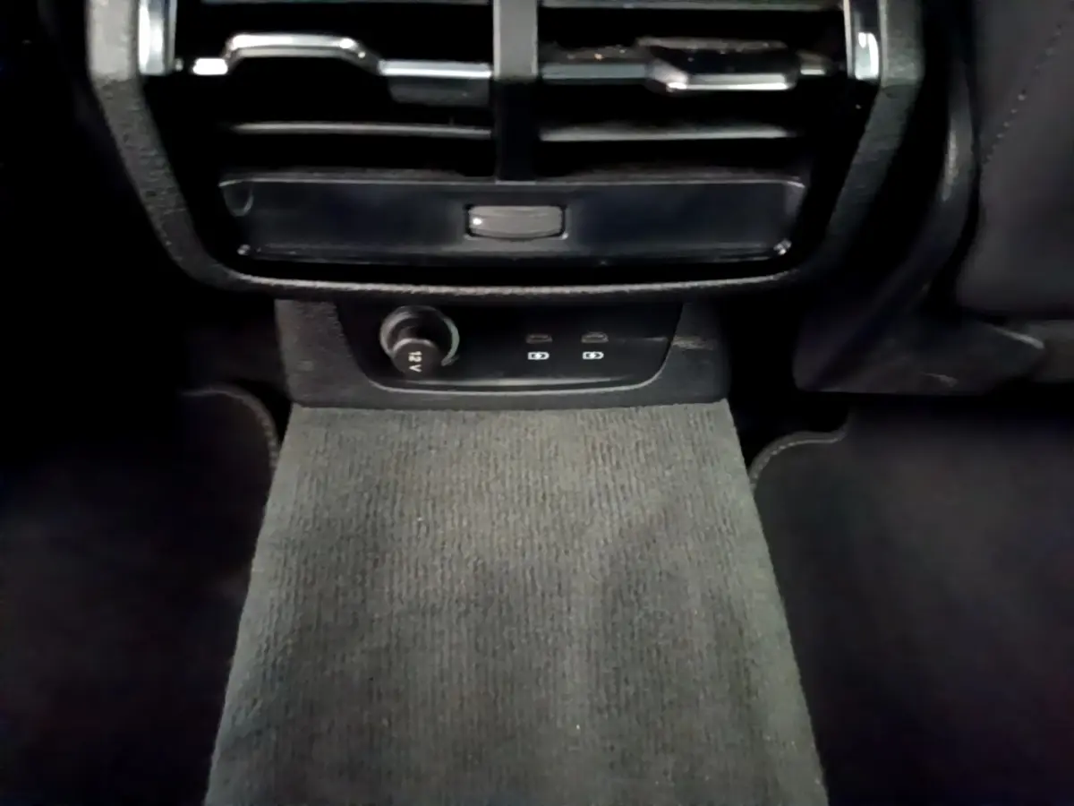 Vue intérieure centrée sur la console arrière noire avec prise 12V et aérateurs dans un Audi Q3 gris foncé.