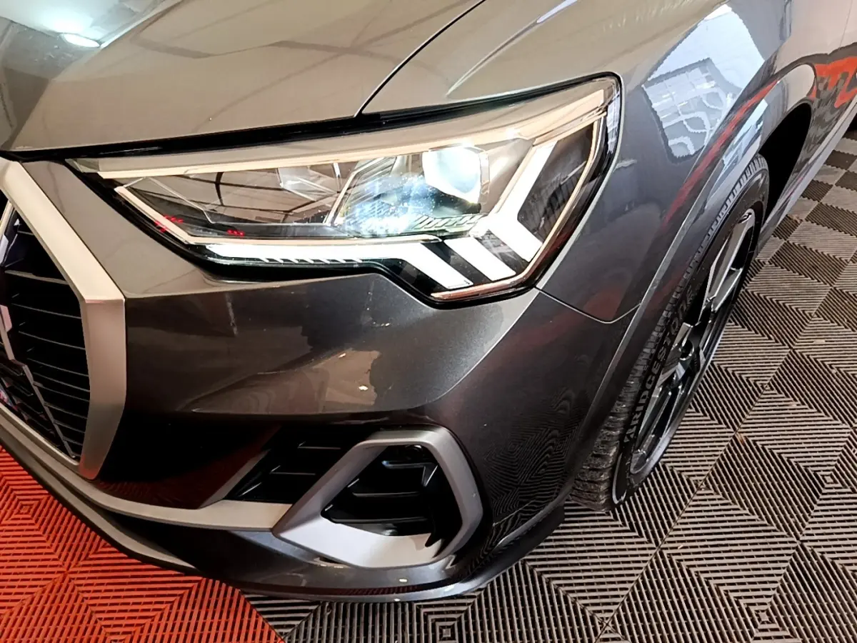 Gros plan sur l'avant droit gris foncé de l'Audi Q3 35 TFSI S LINE, mettant en valeur son phare LED et la calandre.