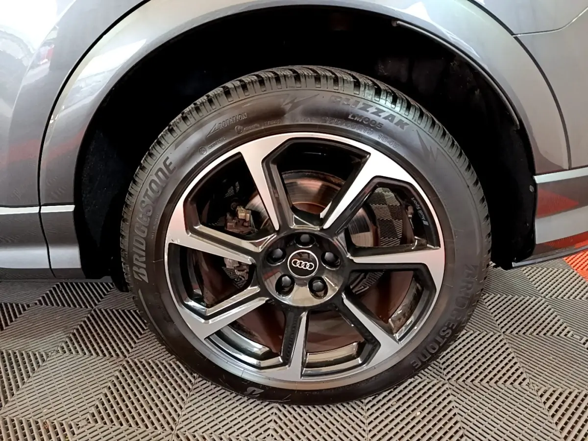 Gros plan sur la roue avant droite d’un Audi Q3 gris foncé avec jante alliage noir et argent.