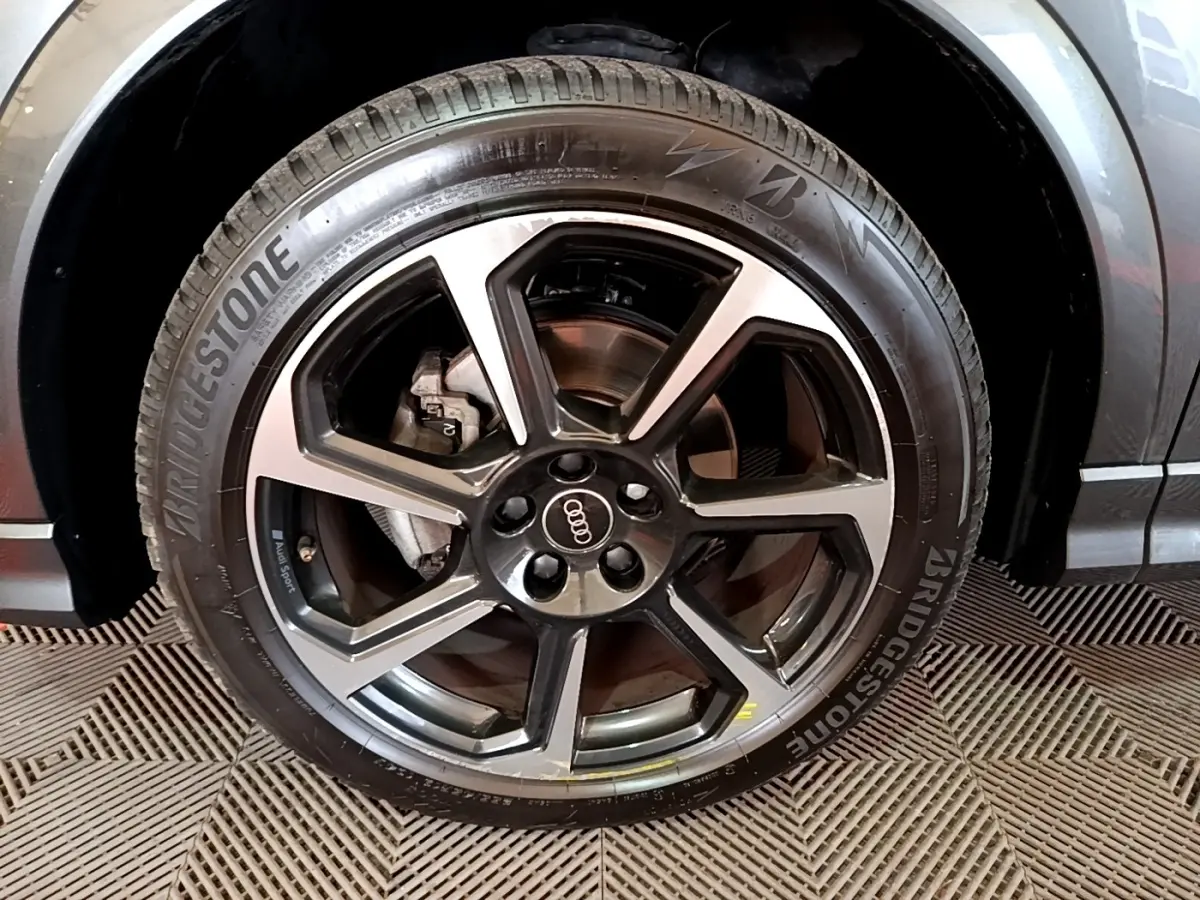 Gros plan sur la roue avant droite d’un Audi Q3 gris foncé avec jante alliage noir et argent et pneu Bridgestone.