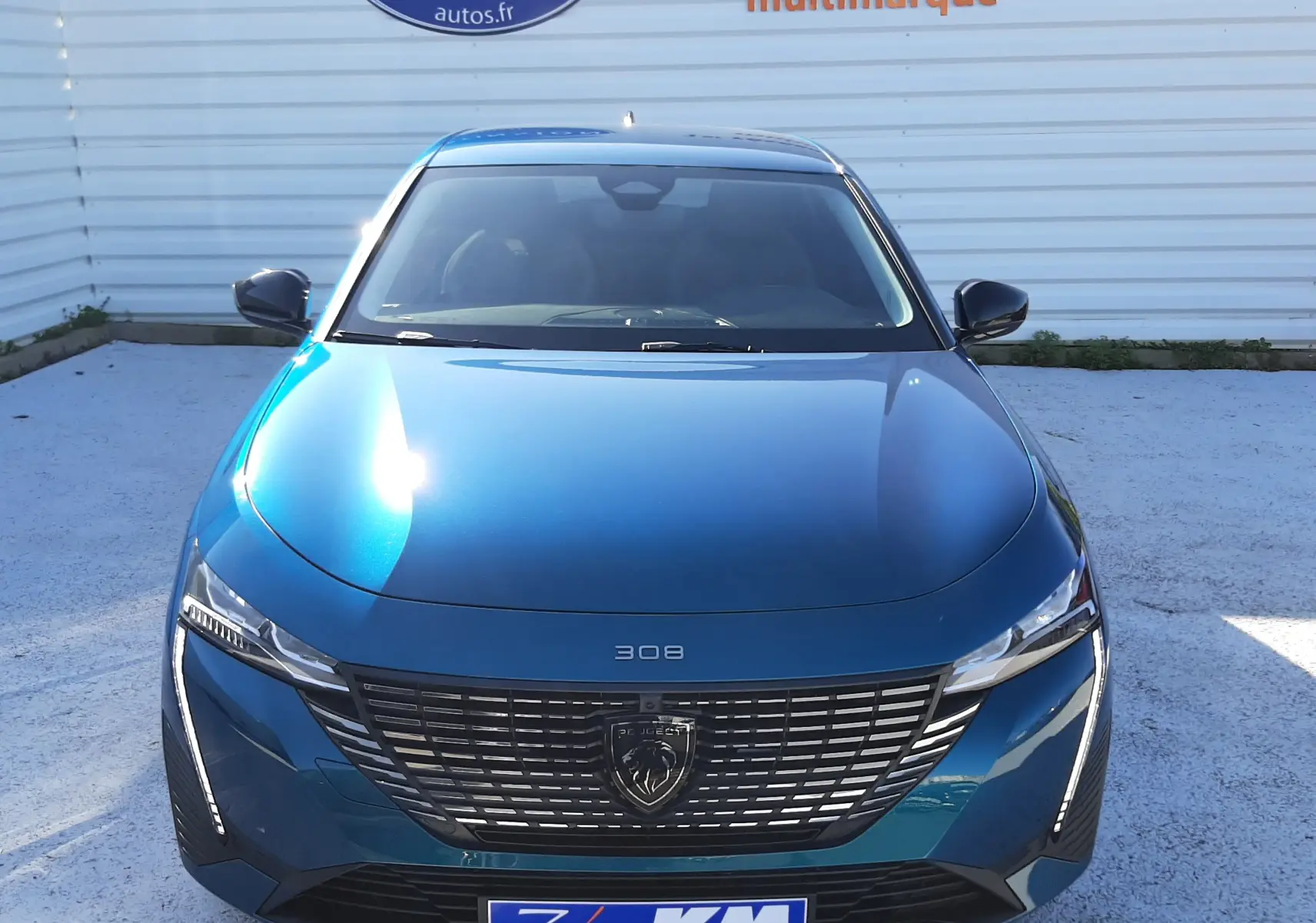 Vue intérieure avant du Peugeot 308 Bleu Obsession avec affichage digital orange sur le pare-brise et fiche tarifaire visible.