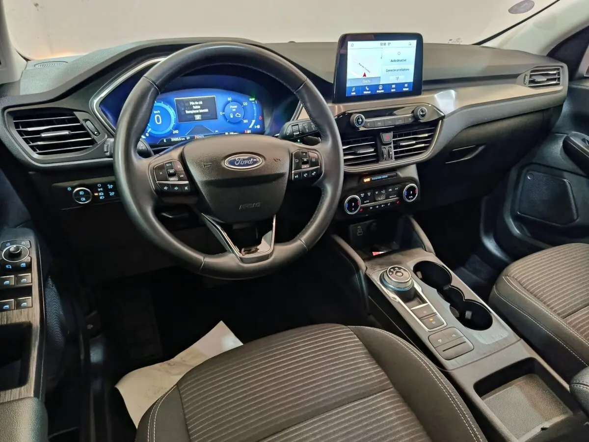 Vue intérieure avant du Ford Kuga 2023 gris foncé, volant cuir multifonctions et écran tactile central visible.