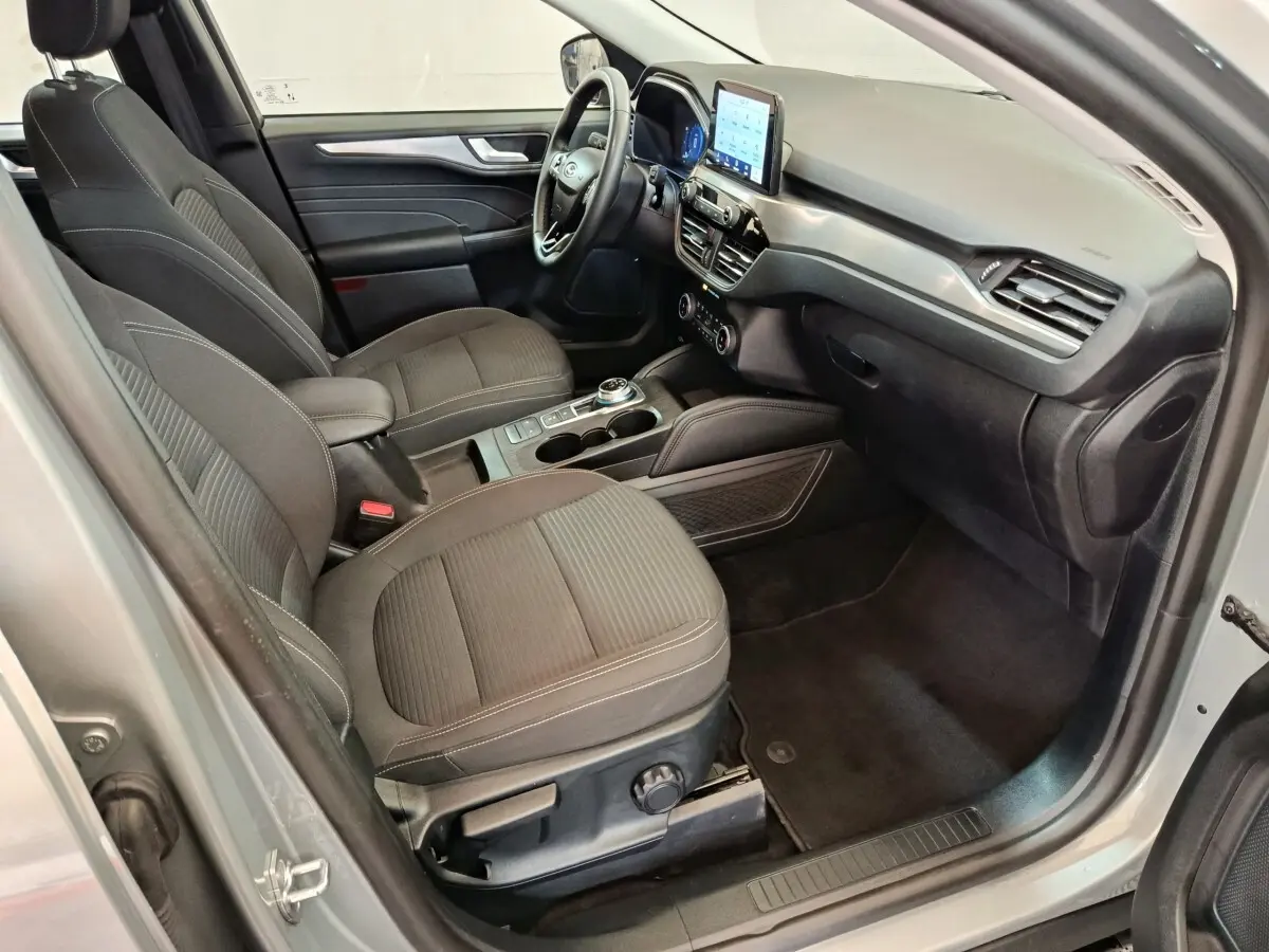 Vue intérieure côté conducteur du Ford Kuga 2023, sièges tissu gris foncé et écran tactile central visible.