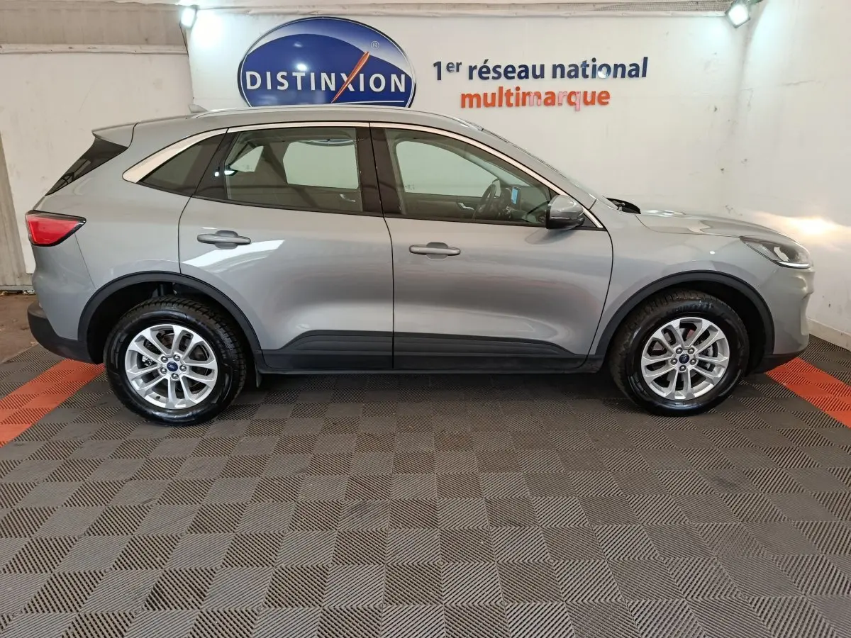 Vue de profil côté gauche d'un Ford Kuga gris foncé 2023 avec jantes alliage et barres de toit chromées.