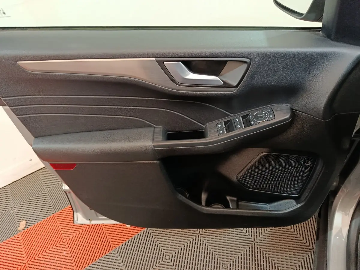 Vue intérieure côté gauche de la porte avant d’un Ford Kuga gris foncé avec commandes de vitres et haut-parleur intégré.