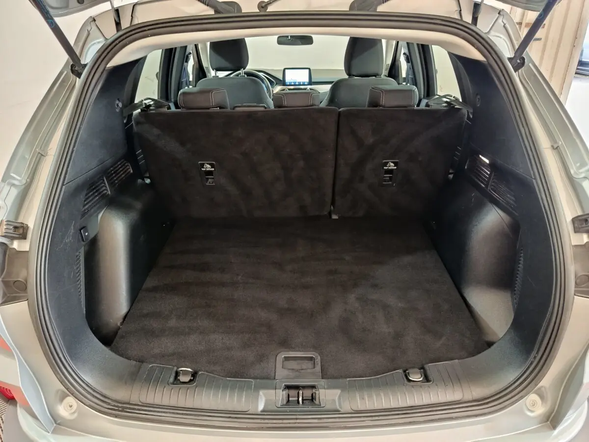 Vue du coffre ouvert d'un Ford Kuga gris foncé 2023, montrant l'espace de chargement et les sièges arrière rabattus.