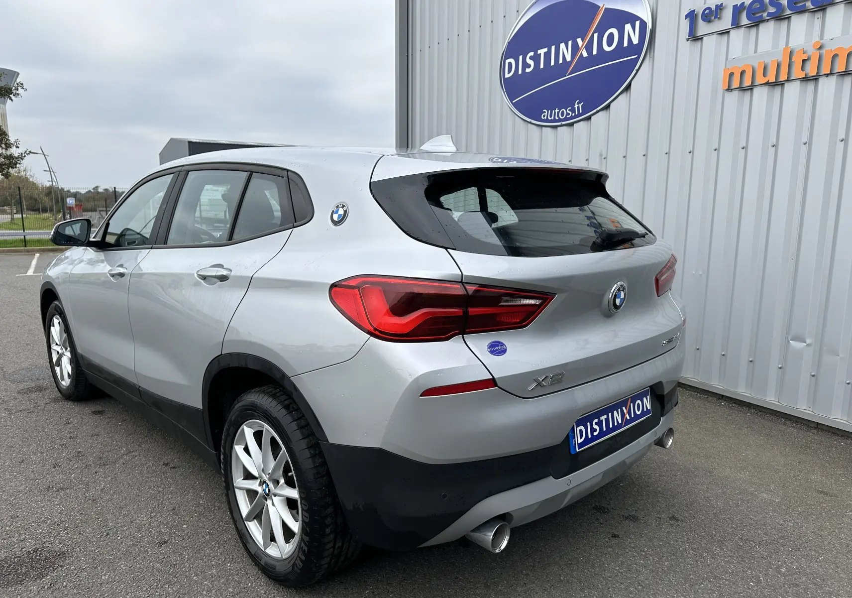 Vue 3/4 arrière droite d'un BMW X2 gris 2018 avec feux LED et double sortie d'échappement visible.