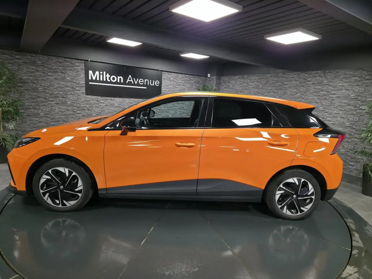 Profil droit d'une MG4 électrique orange avec toit noir et jantes alliage bi-ton dans un showroom intérieur.