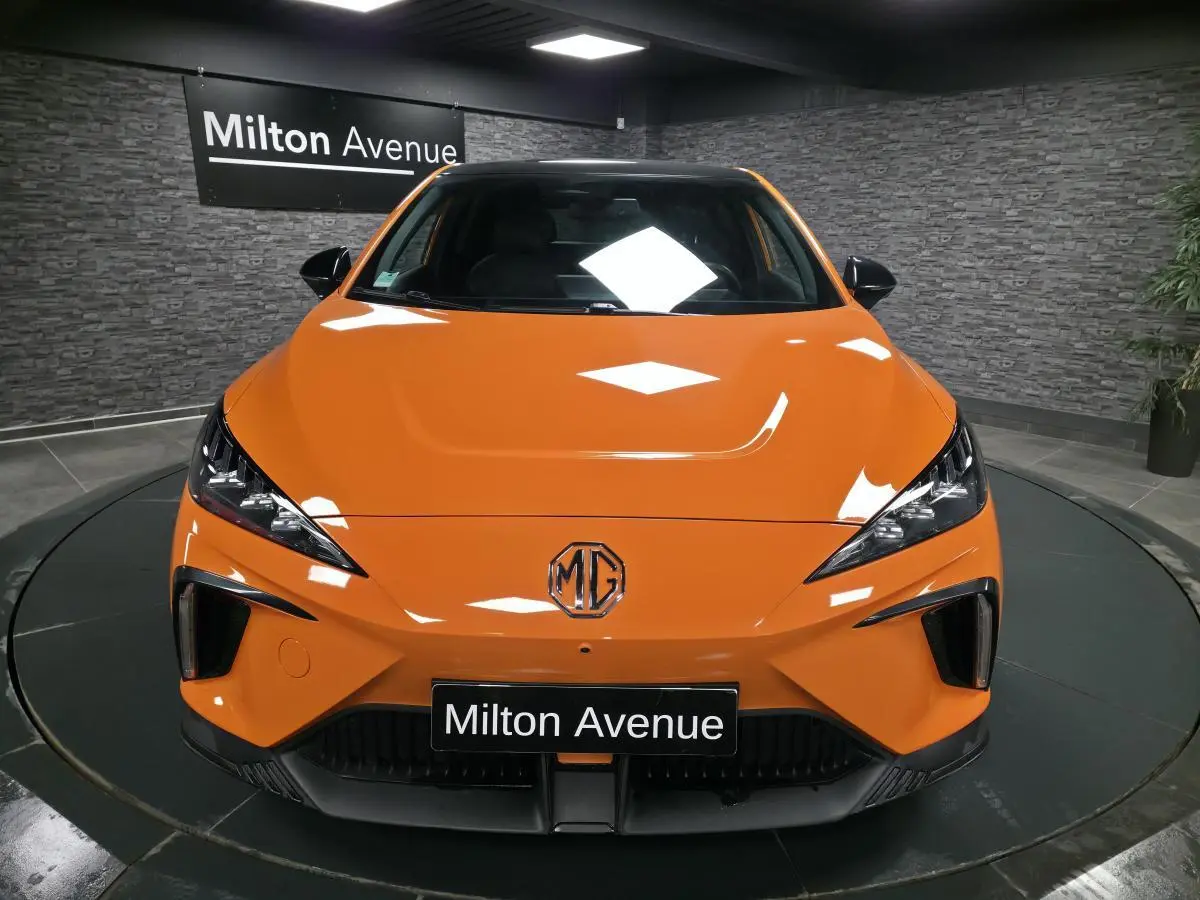 Vue avant d'une MG4 électrique orange avec calandre noire et logo MG centré, en showroom Milton Avenue.