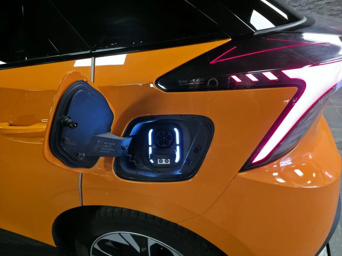 Prise de recharge ouverte côté arrière droit d'une MG4 orange avec feux arrière LED en forme de flèche.