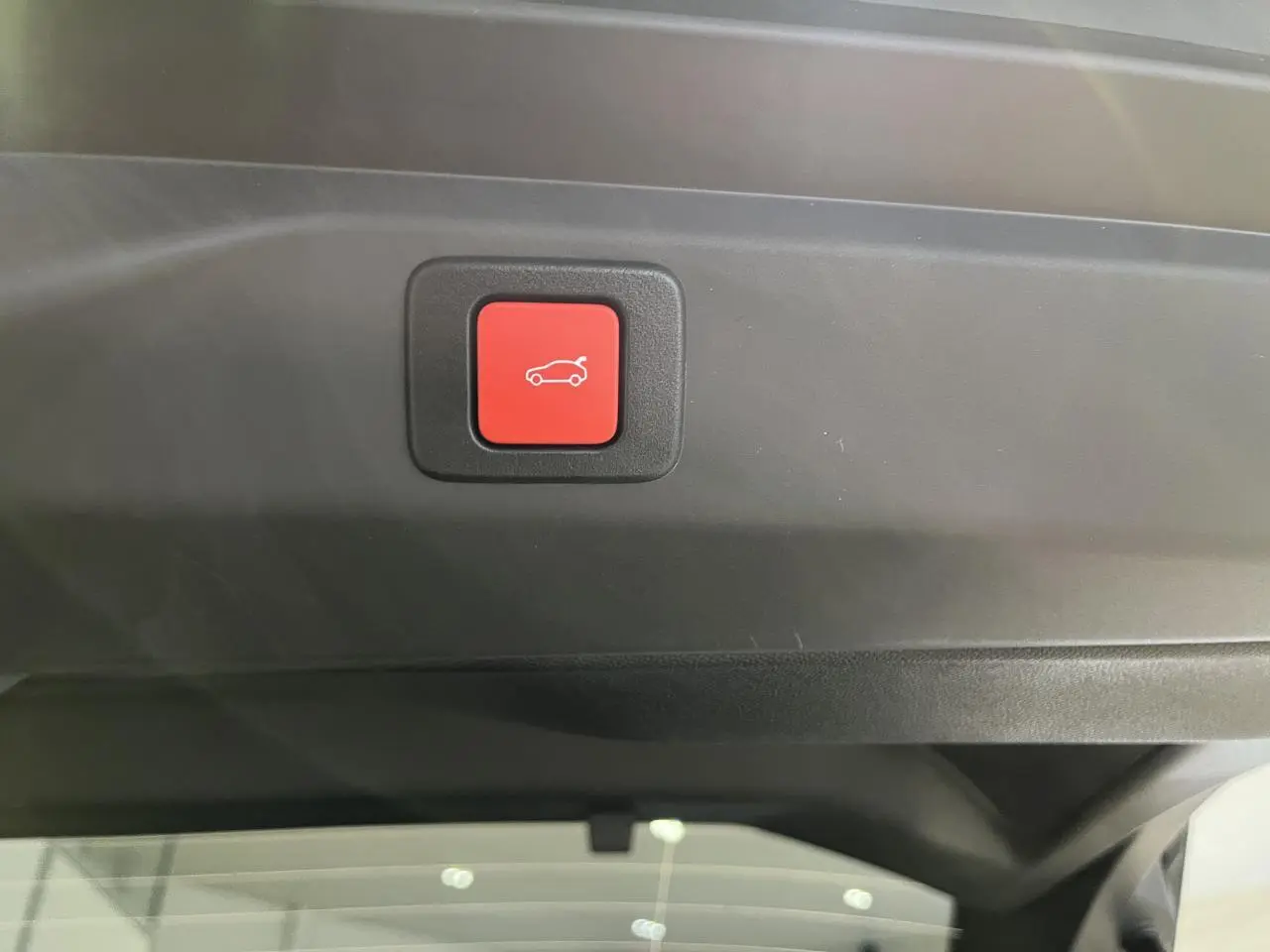 Bouton rouge d'ouverture électrique du hayon sur la garniture intérieure du coffre du Peugeot 3008 gris titanium.