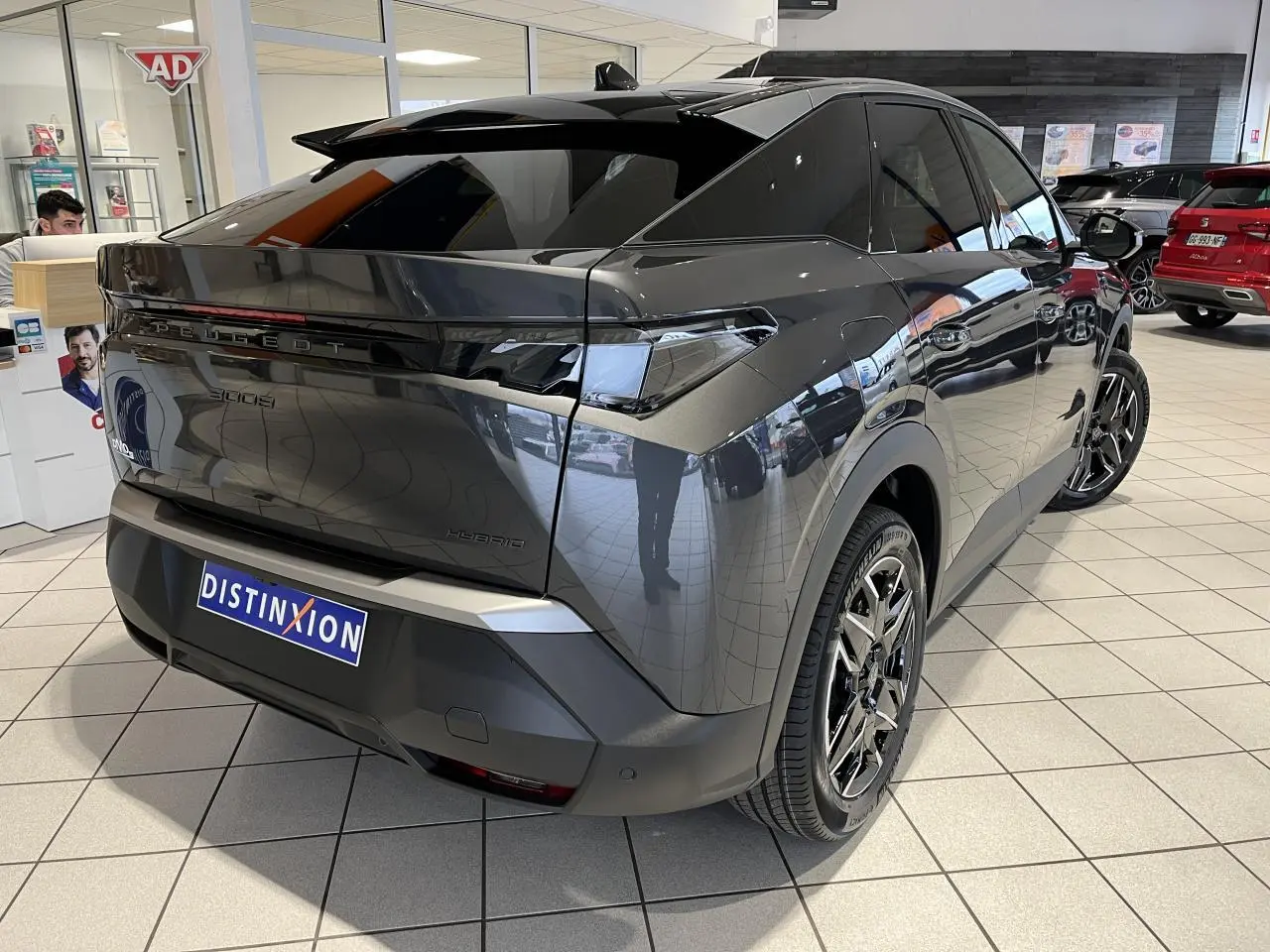 Vue 3/4 arrière droite du Peugeot 3008 Hybrid gris titanium avec jantes alliage 19'' et bandeau noir laqué entre feux arrière.