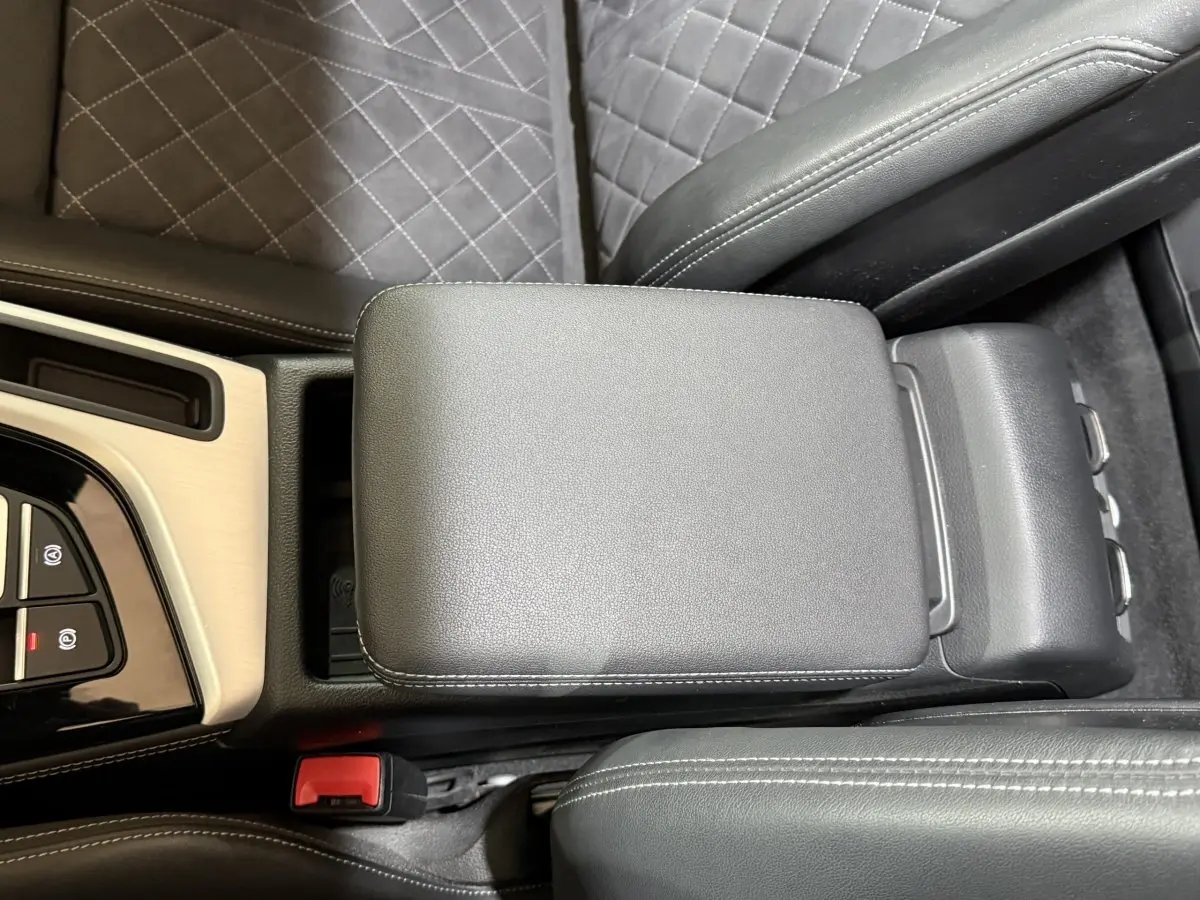 Vue en plongée du couvercle de la console centrale en cuir noir avec surpiqûres blanches de l'Audi A4 gris foncé.