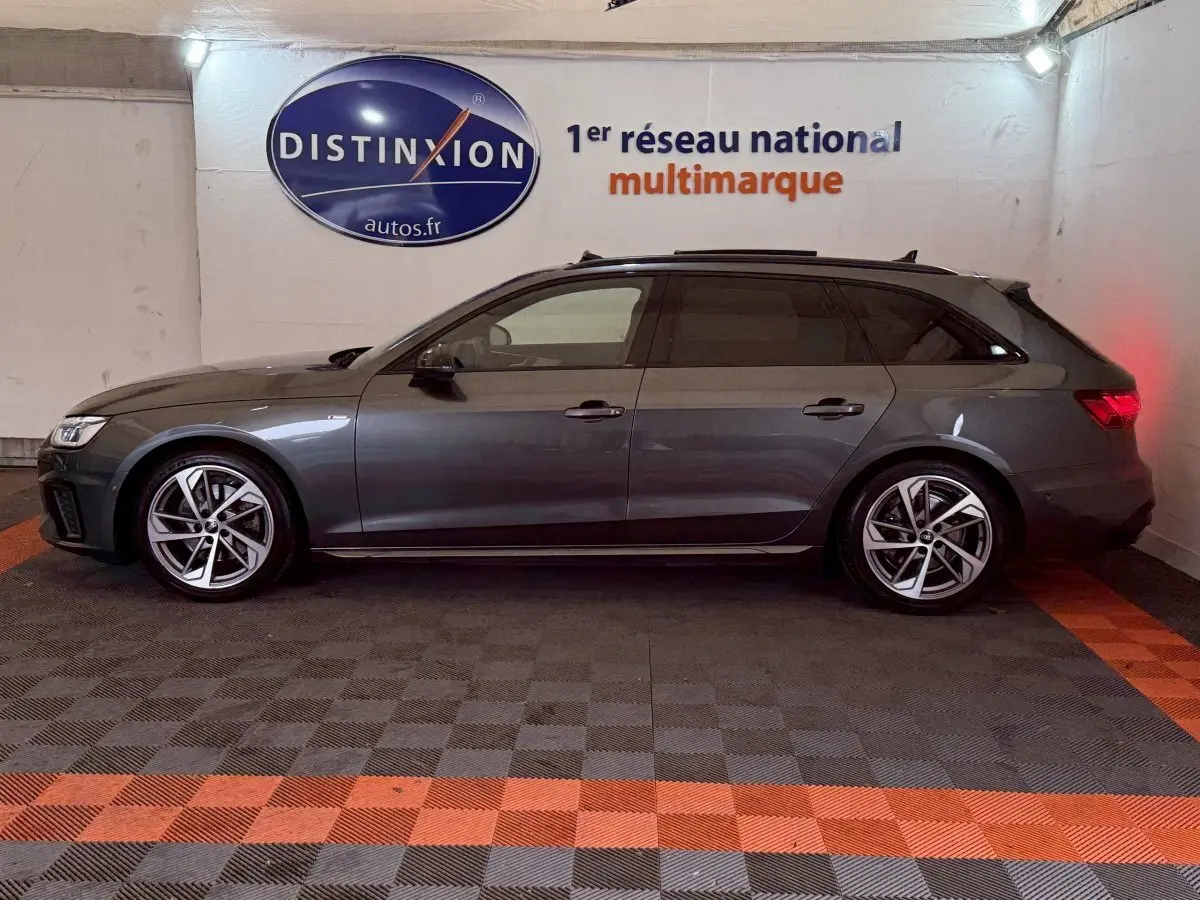 Vue latérale gauche d'une Audi A4 35 TFSI S Edition gris foncé en break, stationnée en intérieur sur sol à damiers.
