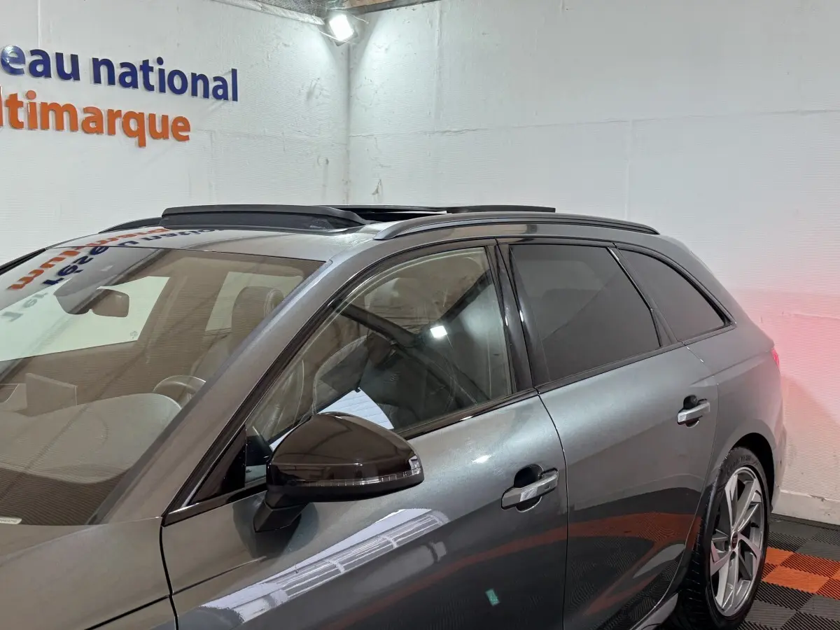 Vue de profil côté gauche d'une Audi A4 gris foncé avec toit ouvrant panoramique en intérieur showroom.