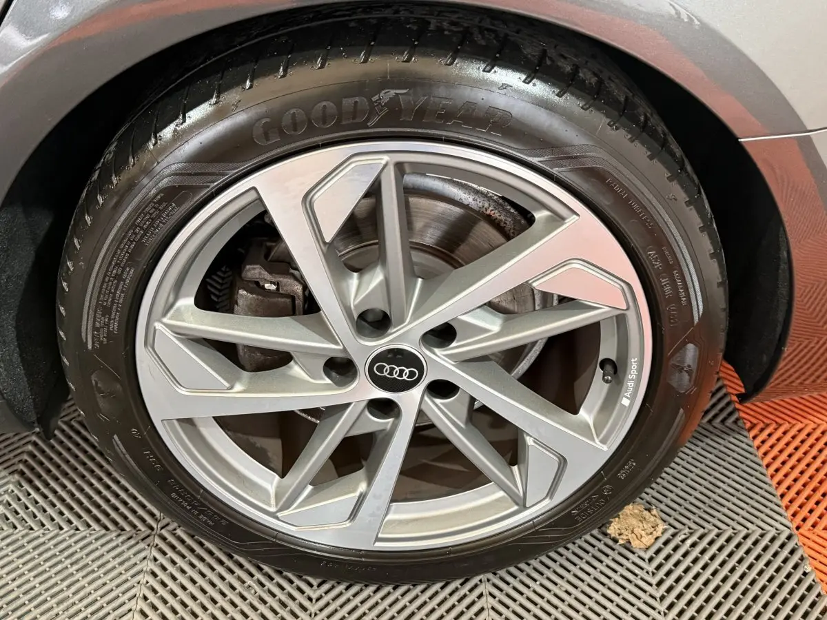 Gros plan sur la jante alliage argentée Audi Sport et pneu Goodyear d'une Audi A4 gris foncé.