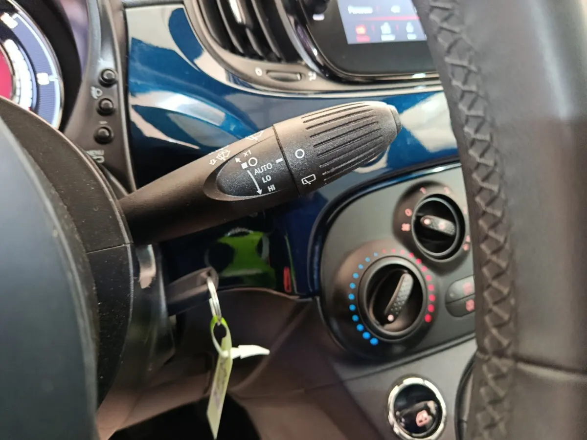 Gros plan sur la commande d’essuie-glace et les réglages de climatisation, tableau de bord bleu de la Fiat 500 Hybrid.