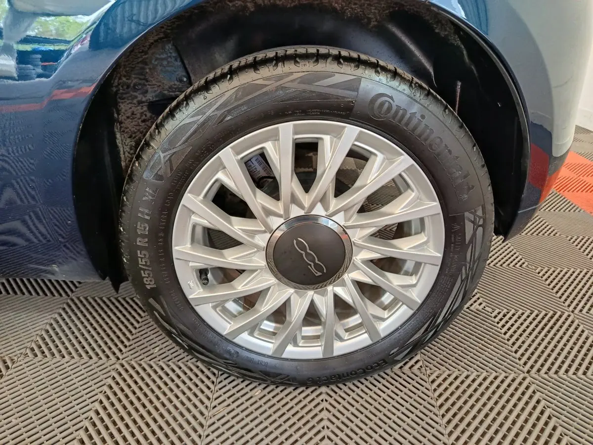 Gros plan sur la roue avant droite d'une FIAT 500 bleu, mettant en valeur la jante argentée au design étoilé.