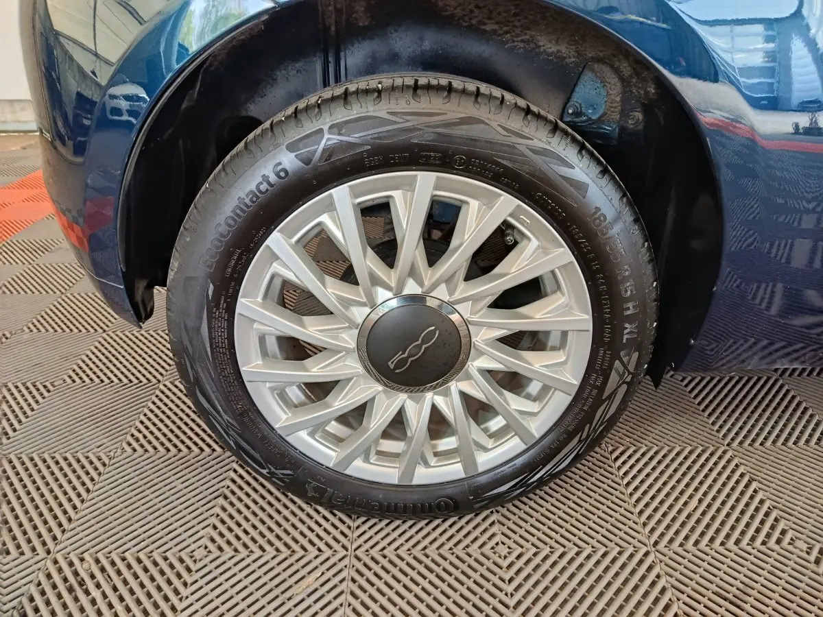Gros plan sur la roue arrière droite d'une FIAT 500 Dolcevita bleu, avec passage de roue et partie de la carrosserie visibles.