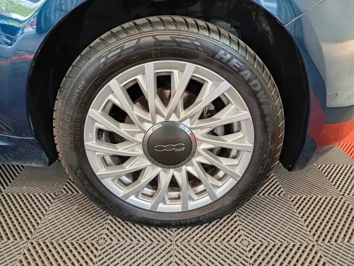 Gros plan sur la roue arrière droite d'une FIAT 500 Hybrid bleu, avec partie de la carrosserie visible.
