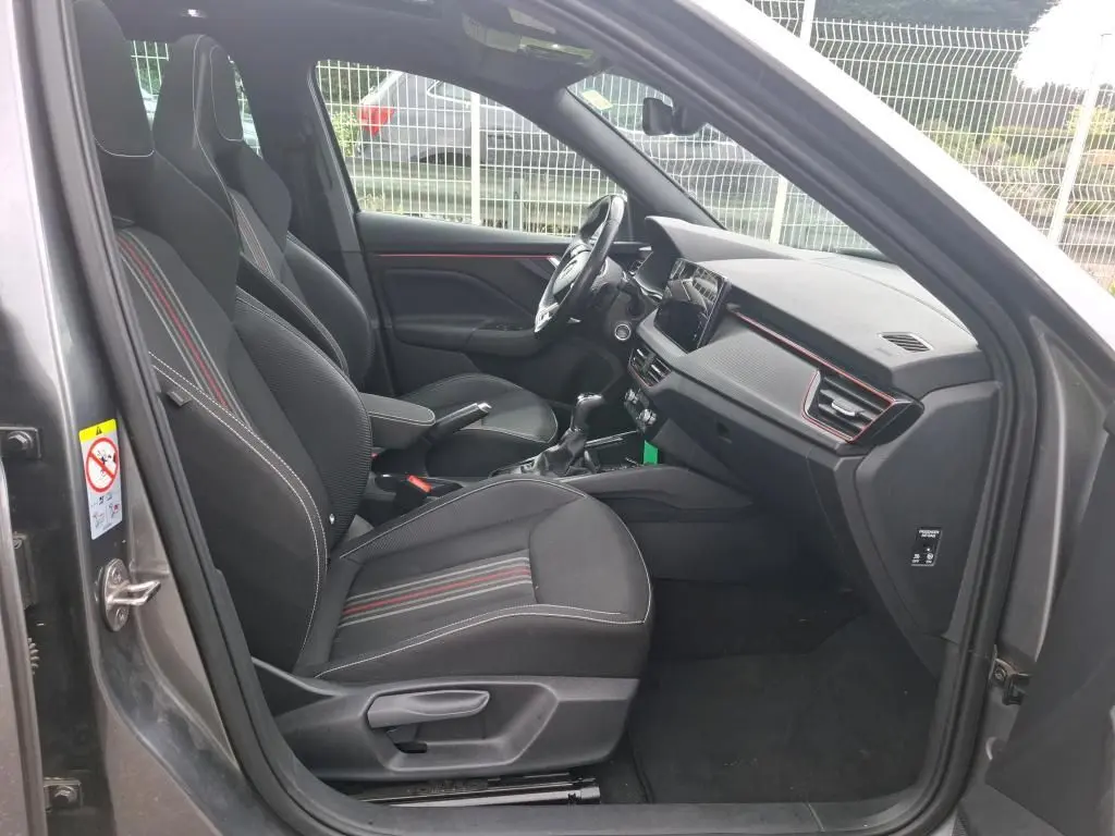 Vue intérieure côté conducteur du Skoda Kamiq gris foncé 2024, sièges tissu noir avec surpiqûres rouges et tableau de bord moderne.