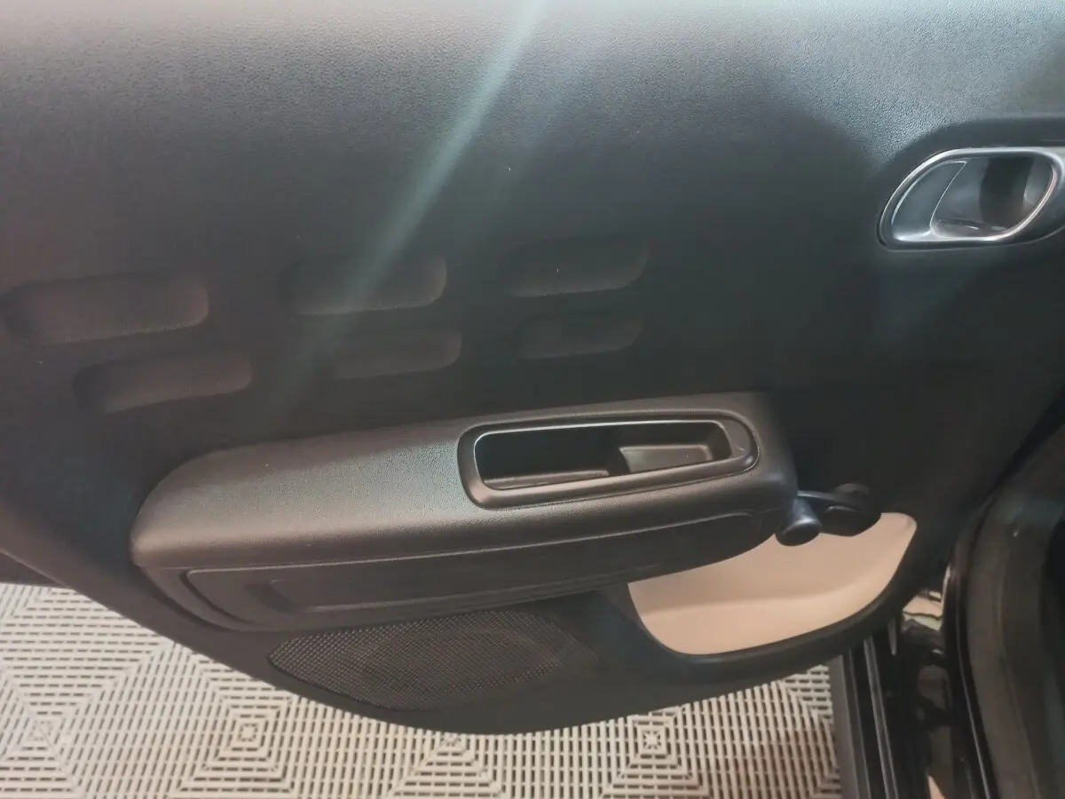Vue rapprochée de la porte intérieure côté droit de la Citroën C3 noire, avec poignée et manivelle de vitre manuelle.