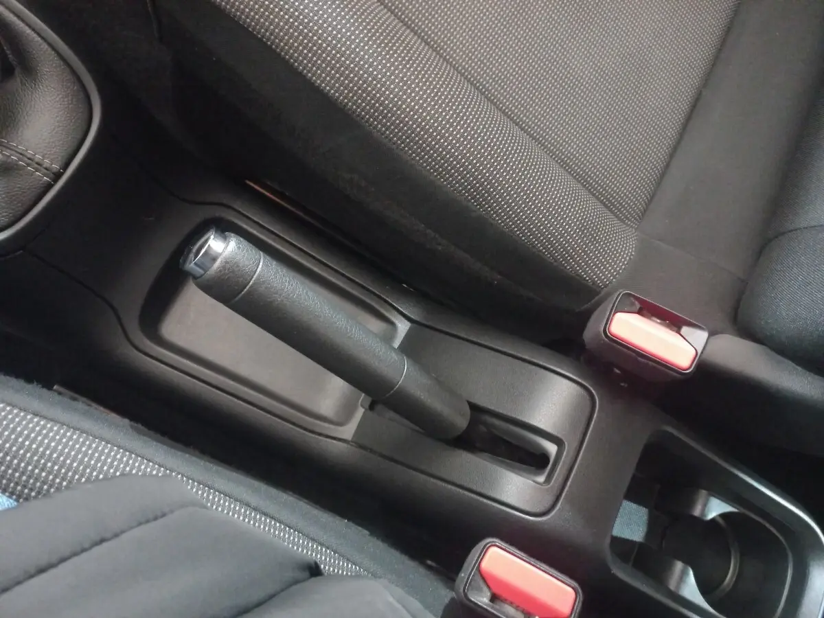 Vue rapprochée de la console centrale noire de la Citroën C3 2024, avec frein à main manuel et ceintures rouges.