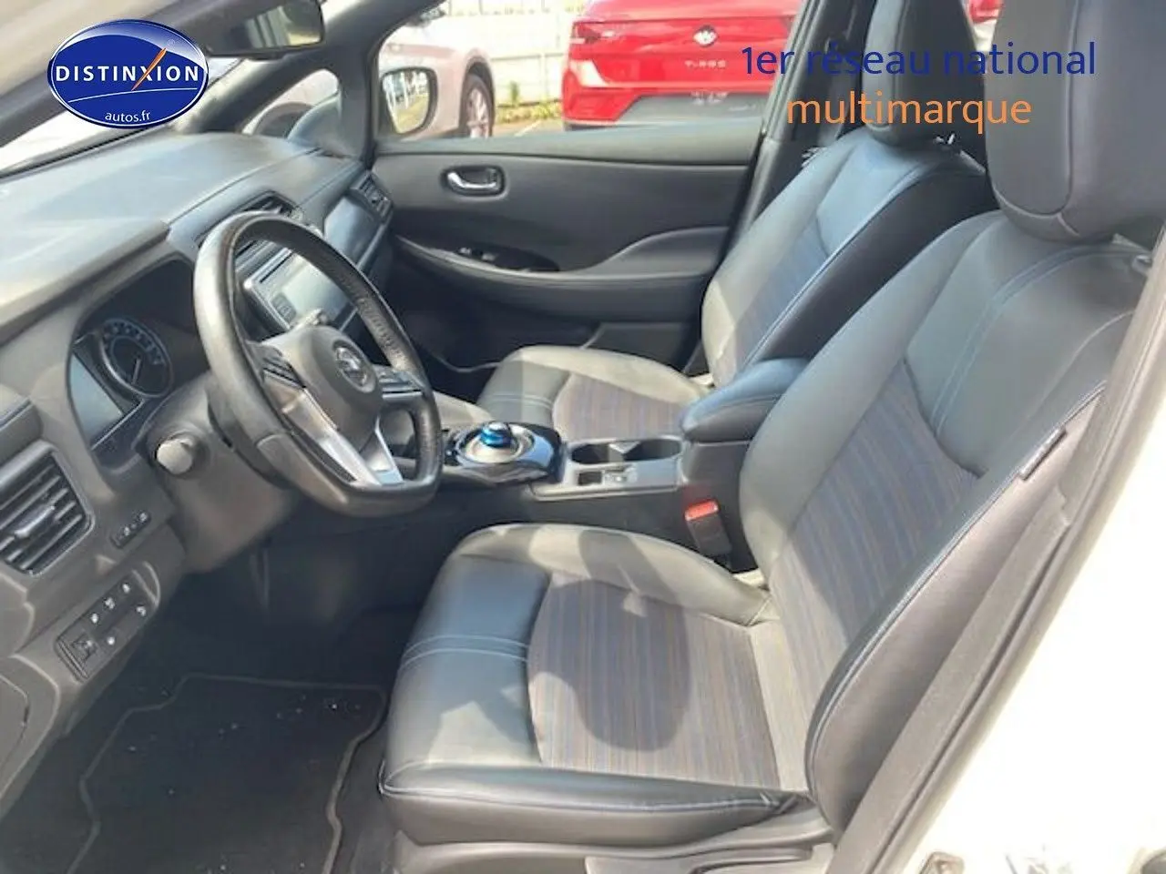 Intérieur du Nissan Leaf électrique blanc nacré, vue côté conducteur sur les sièges en cuir et tableau de bord moderne.