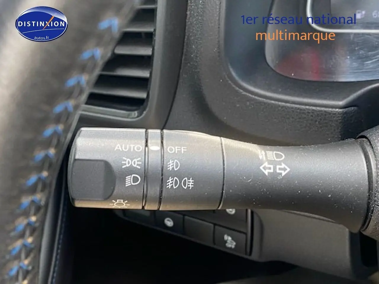 Gros plan sur la commande des feux et clignotants à gauche du volant d'une Nissan Leaf blanche nacrée électrique.