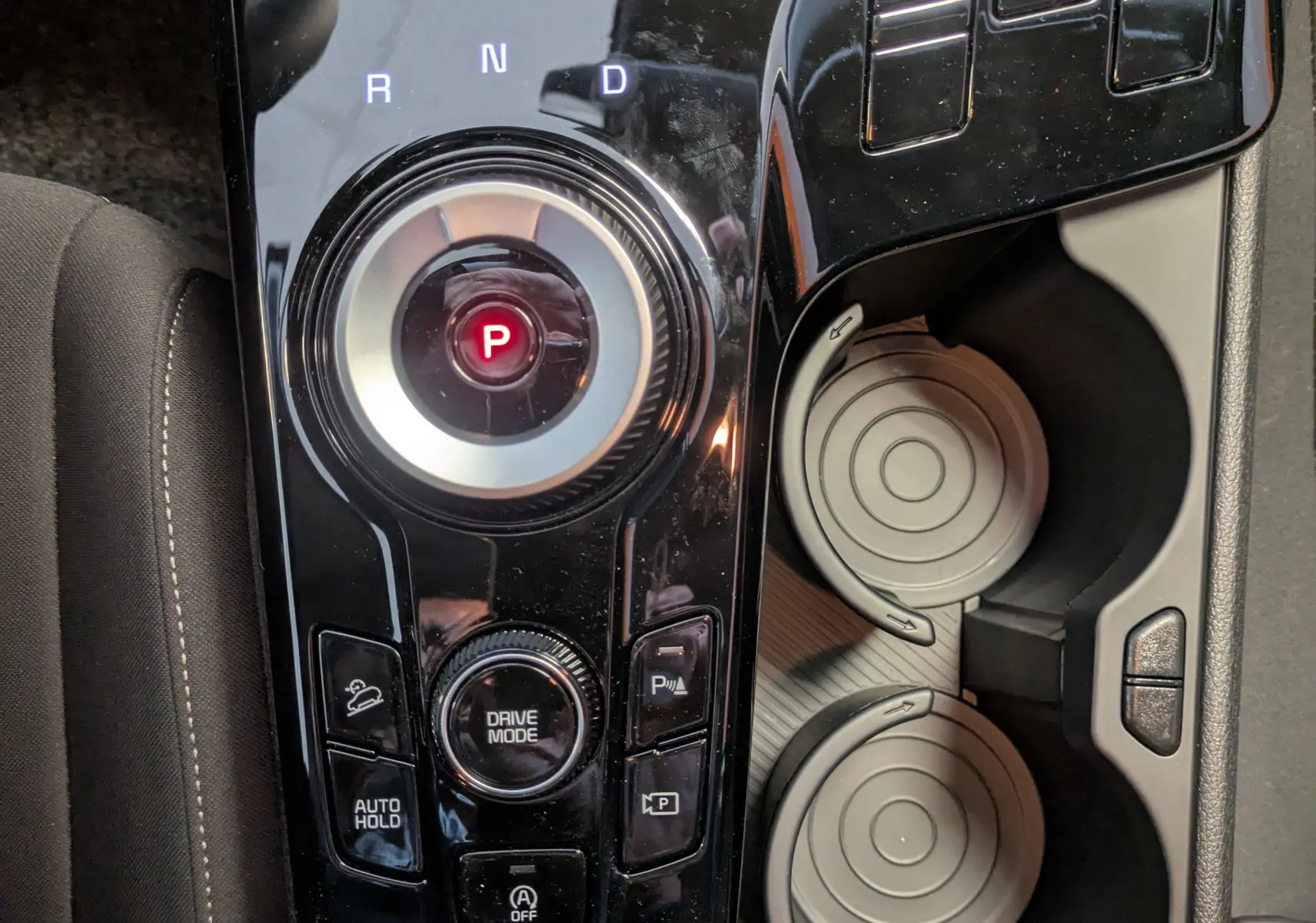 Vue rapprochée de la console centrale noire du Kia Sportage MY25 avec sélecteur rotatif de boîte auto et porte-gobelets.