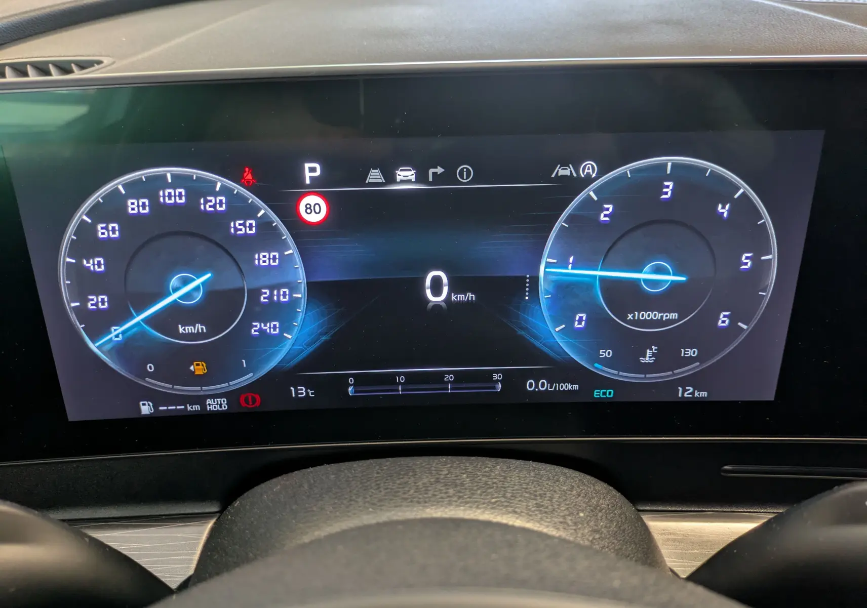 Tableau de bord numérique du Kia Sportage blanc MY25, affichant vitesse, régime et alertes à 0 km/h.