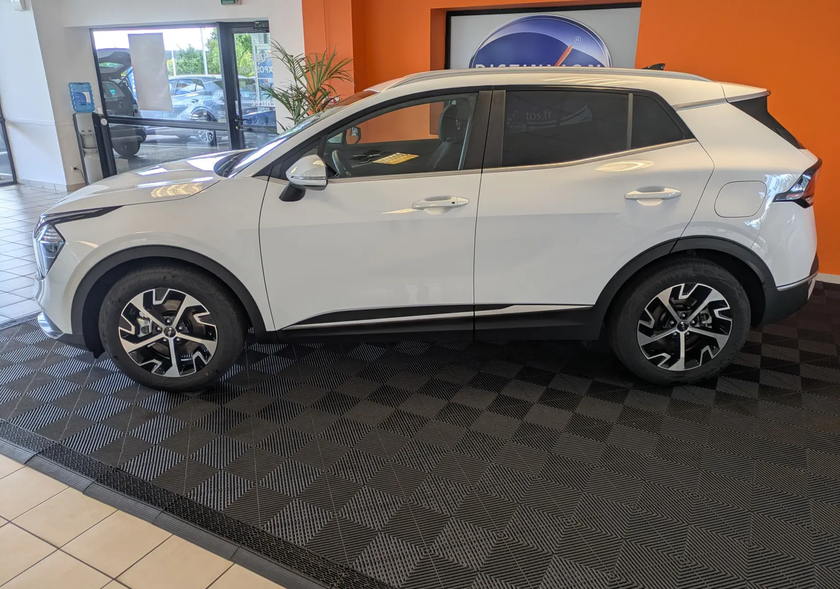 Profil droit du KIA SPORTAGE blanc MY25 avec jantes alliage 18’’ et rétroviseurs rabattables électriquement en showroom.