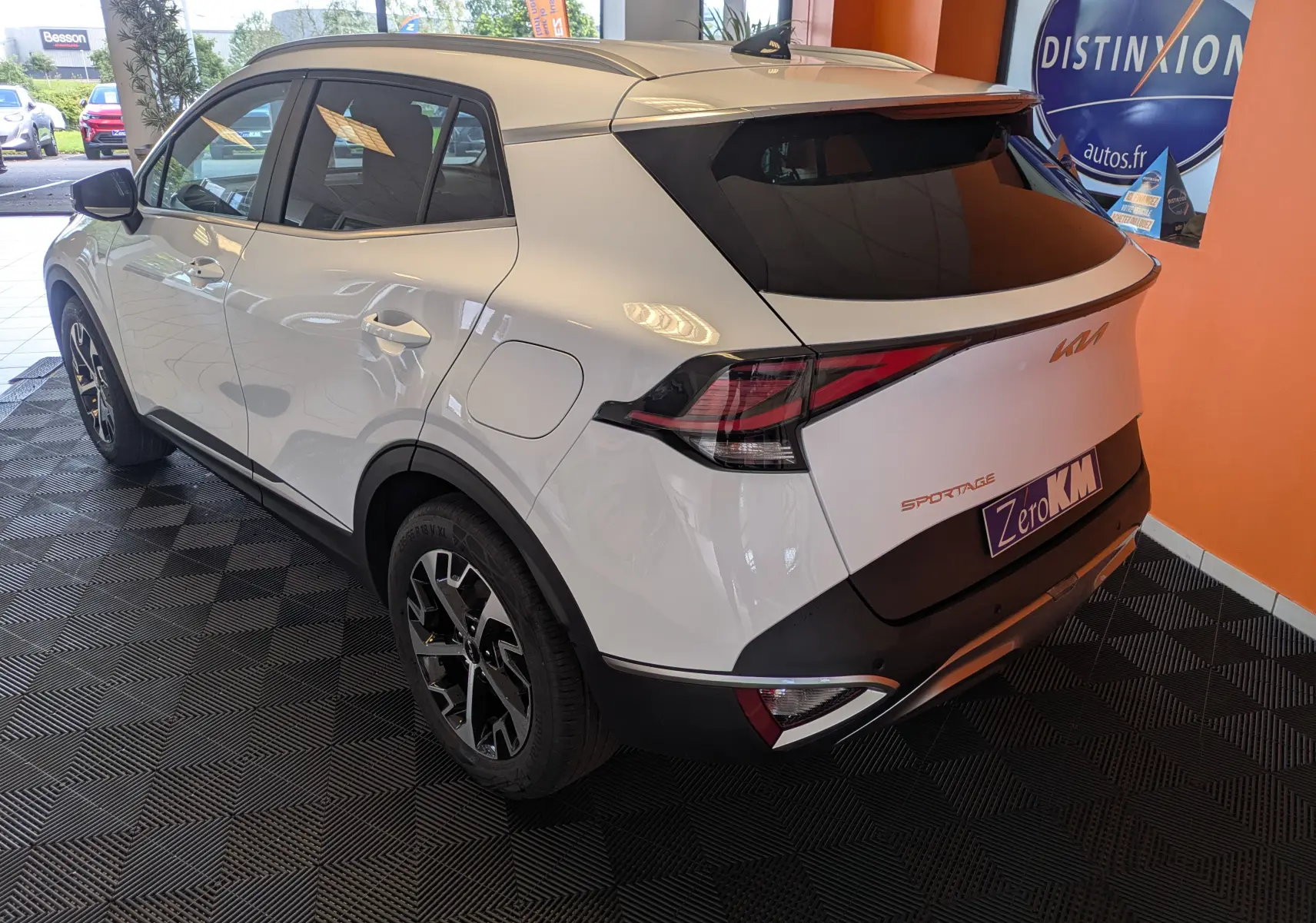 Vue 3/4 arrière droite du SUV blanc KIA Sportage MY25 avec jantes alliage bicolores et vitres teintées en showroom.