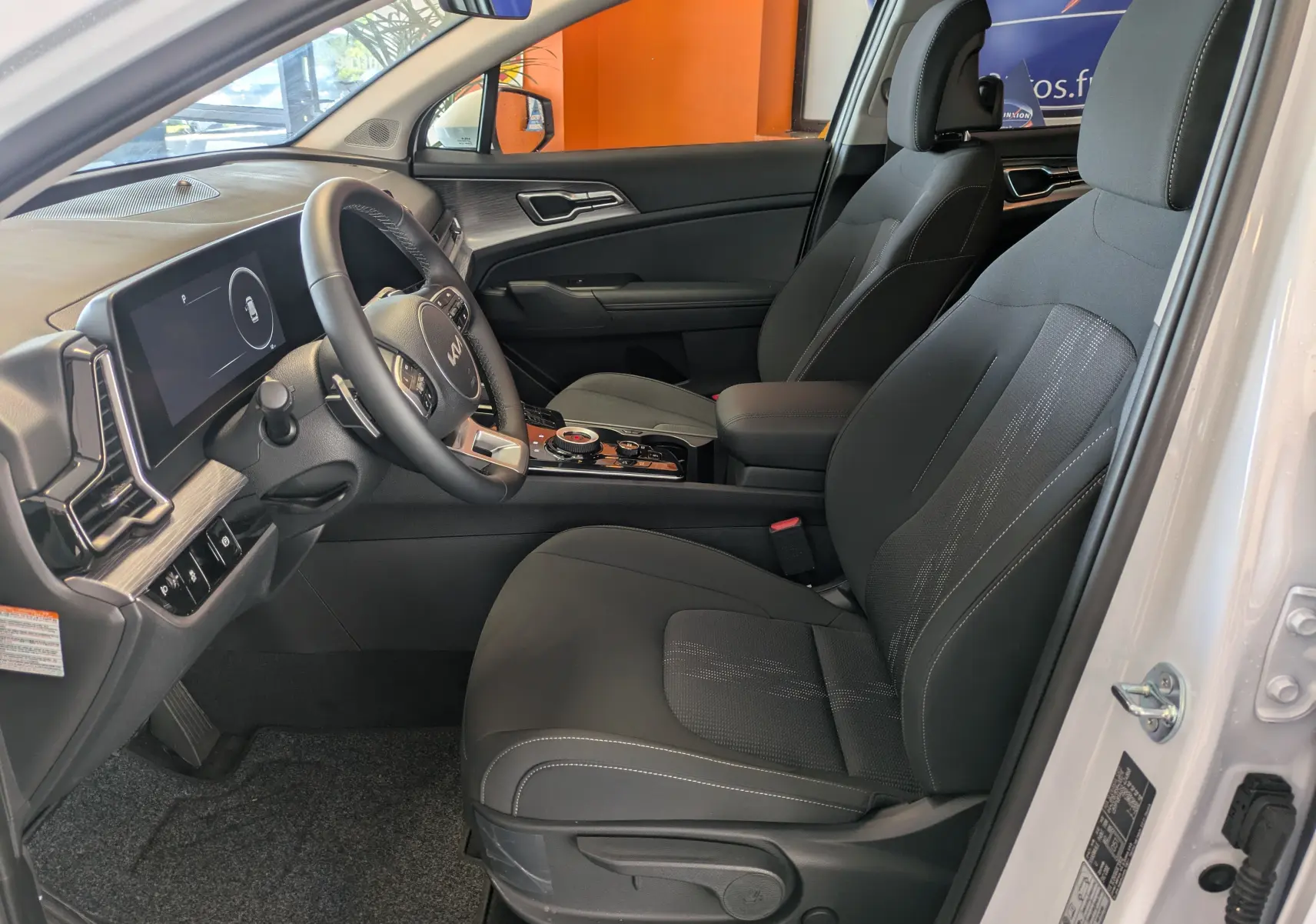 Vue intérieure côté conducteur du Kia Sportage blanc 2025, avec sièges noirs, volant multifonction et écran tactile 12,3 pouces.