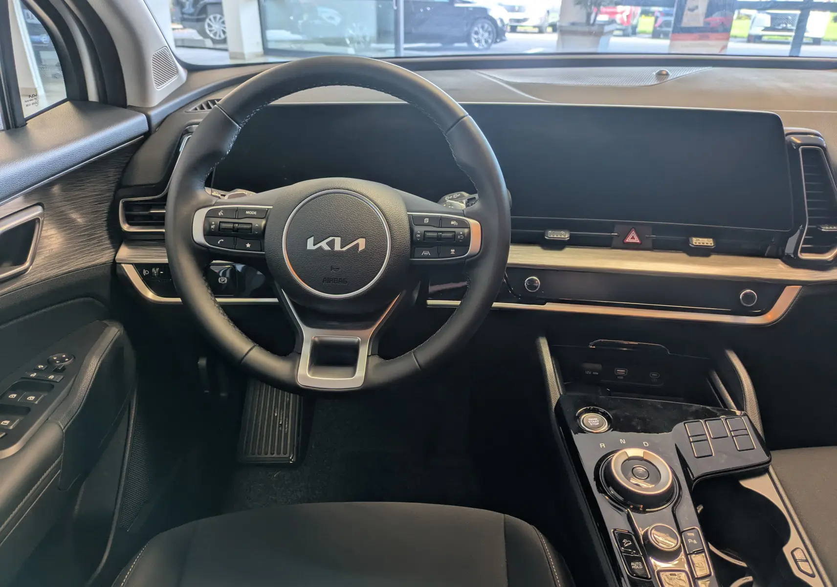 Vue intérieure du tableau de bord et volant noir du KIA SPORTAGE MY25, avec écran tactile large et console centrale moderne.