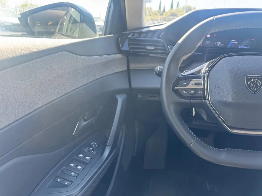 Vue intérieure côté conducteur de la Peugeot 308 Hybrid gris, avec volant multifonction et commandes sur porte.