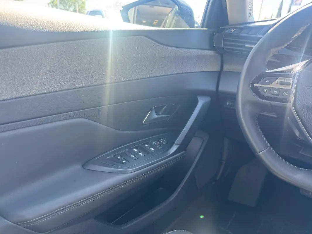 Intérieur côté conducteur de la Peugeot 308 Hybrid gris, montrant la portière avec commandes électriques et partie du volant.