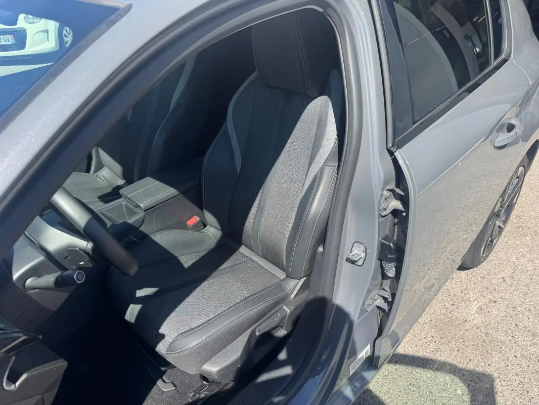 Vue intérieure côté conducteur d'une Peugeot 308 gris 2025, mettant en valeur le siège réglable en hauteur et l'accoudoir central.