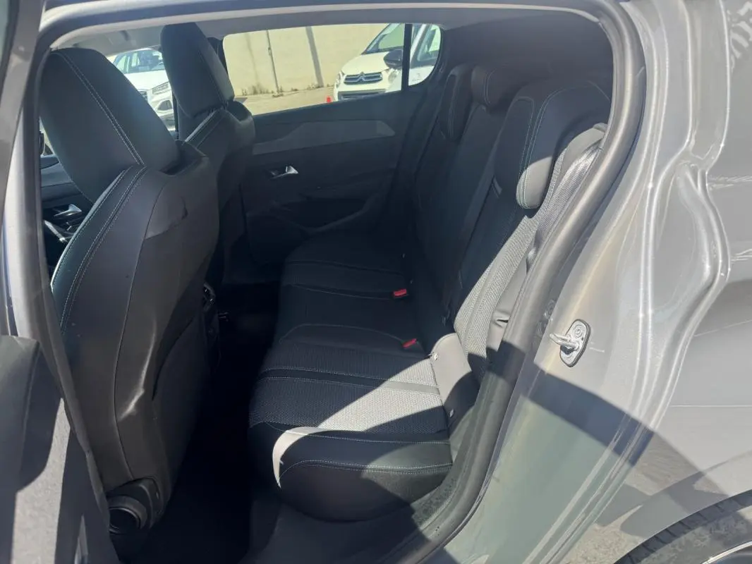Vue intérieure côté droit des sièges arrière noirs de la Peugeot 308 Hybrid gris 2025 avec portes ouvertes.