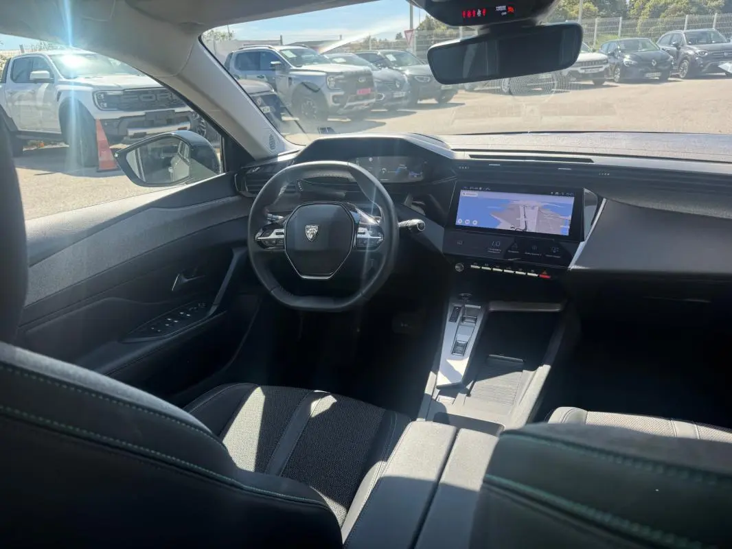 Vue intérieure avant de la Peugeot 308 Hybrid gris, mettant en valeur le volant, le cockpit numérique et l'écran tactile central.