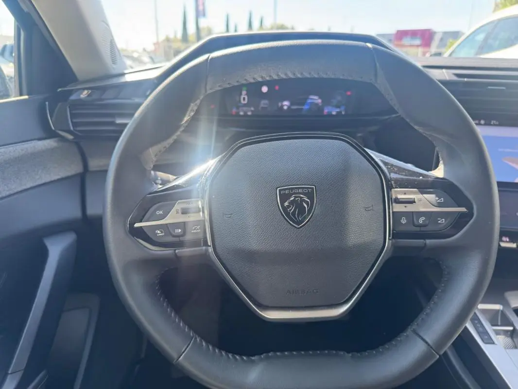 Vue rapprochée du volant cuir noir de la Peugeot 308 Hybrid 136 e-DCS6 Allure avec commandes intégrées et tableau de bord numérique.