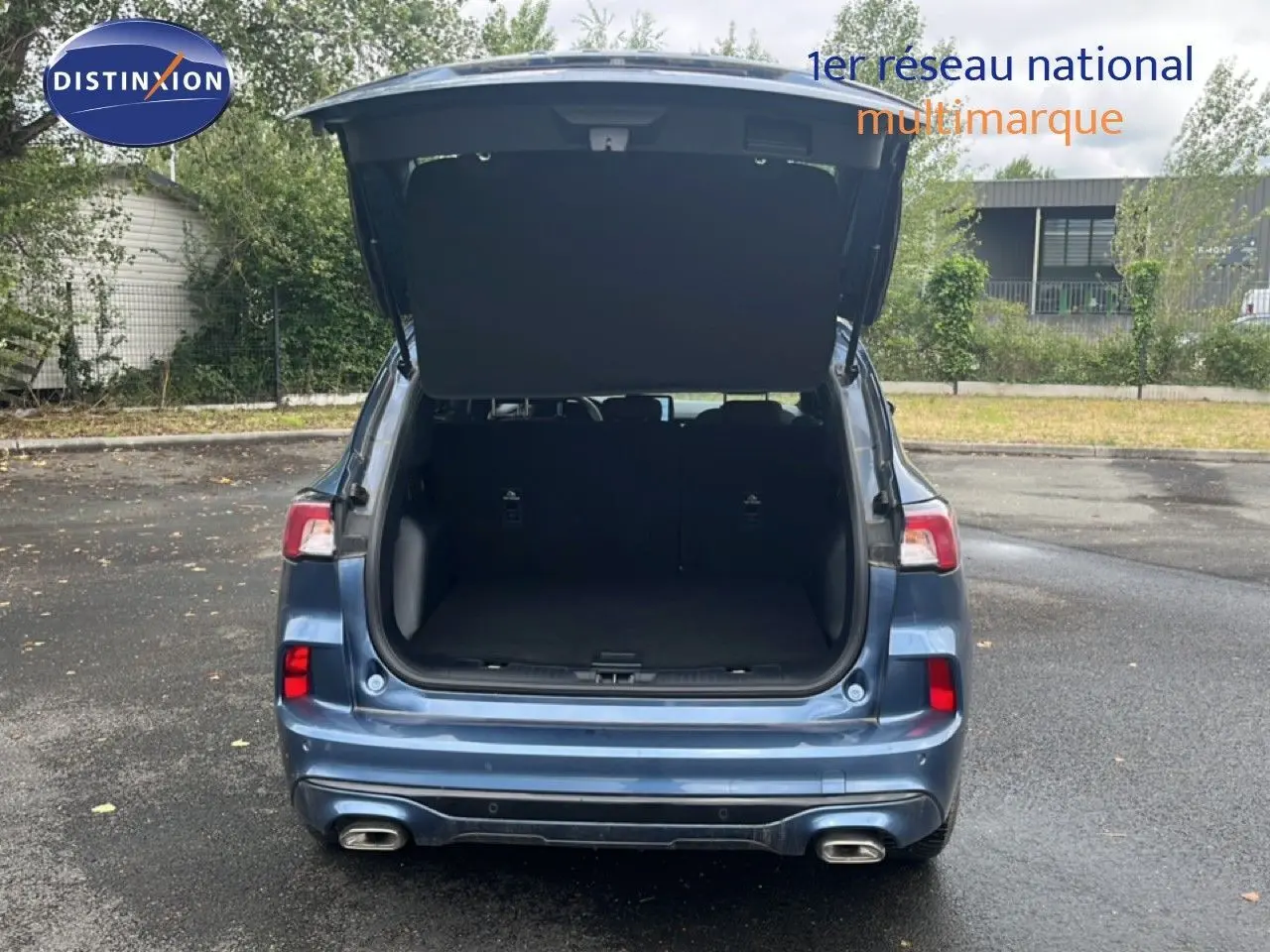 Vue arrière d'un Ford Kuga 2024 bleu chrome métal avec coffre ouvert et double sortie d'échappement visible.