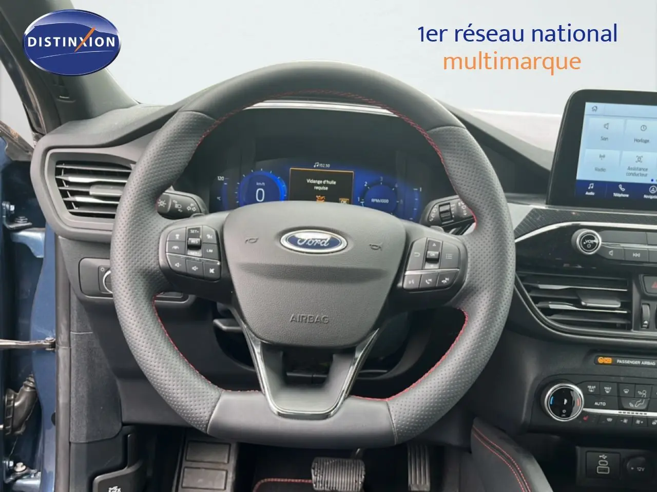 Vue rapprochée du volant cuir noir avec surpiqûres rouges et tableau de bord numérique du Ford Kuga bleu chrome 2024.
